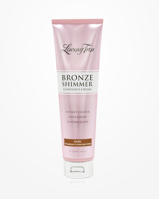 A tube of Loving Tan's Bronze Shimmer Luminous Cream is showcased against a white backdrop. The light pink packaging features text highlighting its ability to provide "instant colour," a "satin finish," and a "luminous glow" for medium to dark skin tones, enhancing your natural radiance.